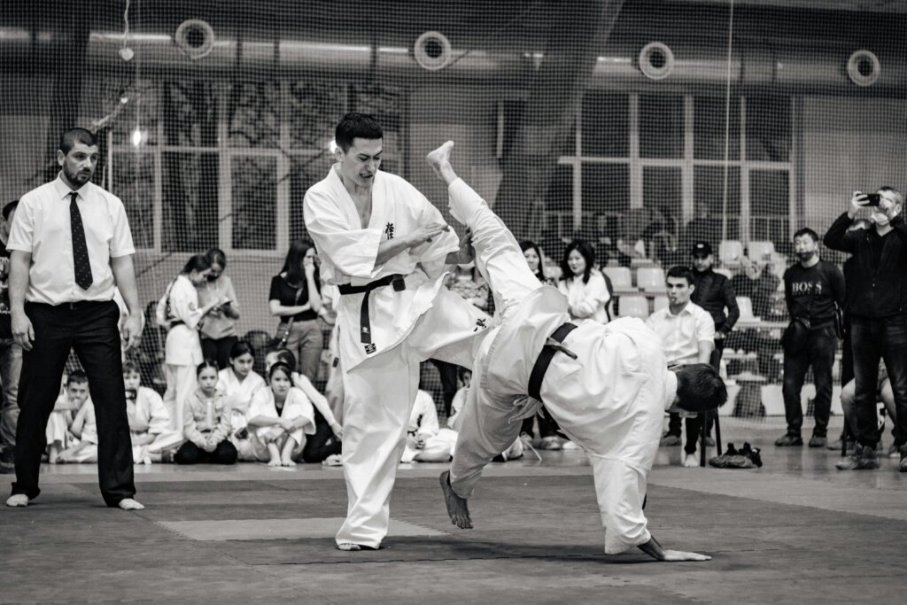 Black and white action shot of a karate match at a tournament, showcasing skillful combat.