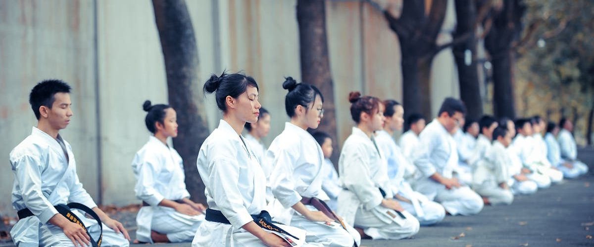 Group of martial artists practicing meditation and focus outdoors, dressed in traditional gis.